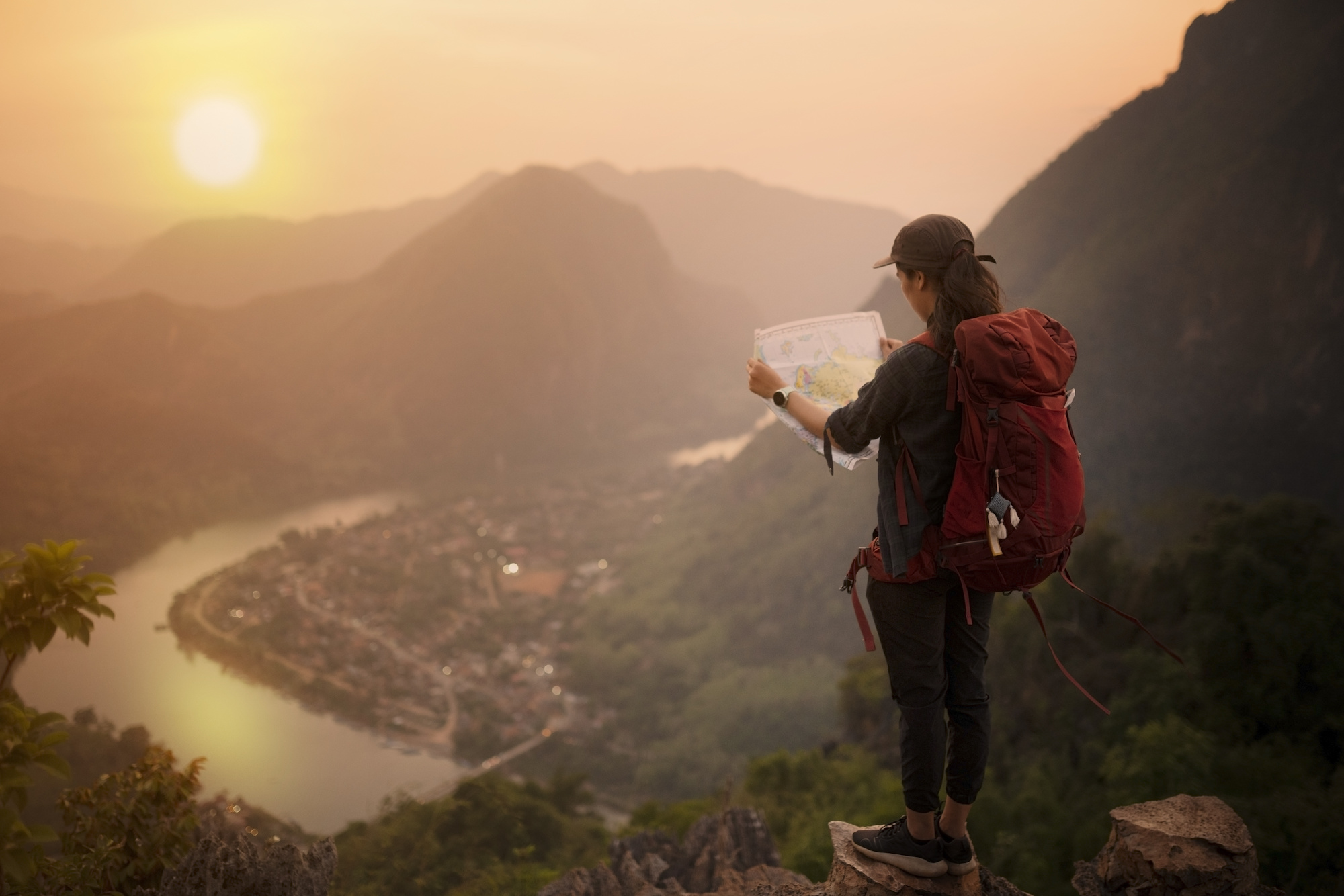 Backpacker woman standing on top of mountain and looking map with nature background